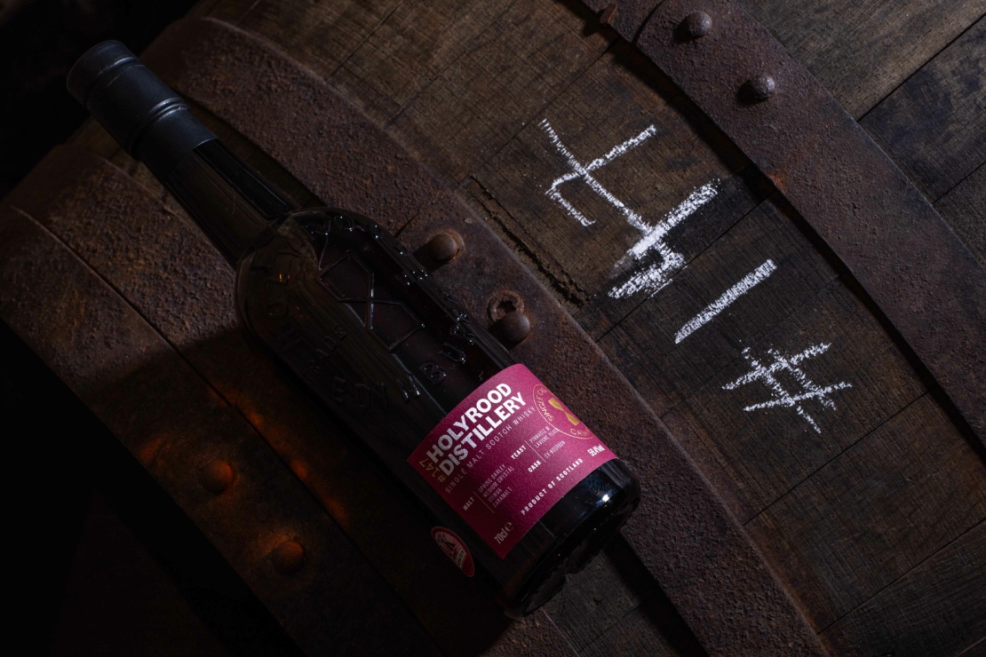 Bottle of Holyrood Distillery Single Cask Whisky laying flat on a whisky cask.