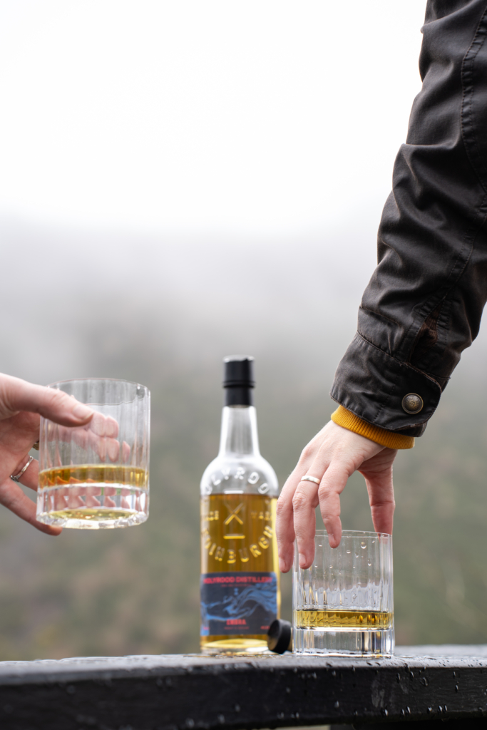 Two people raising glasses of whisky, with a bottle of Scotch Whisky in the background